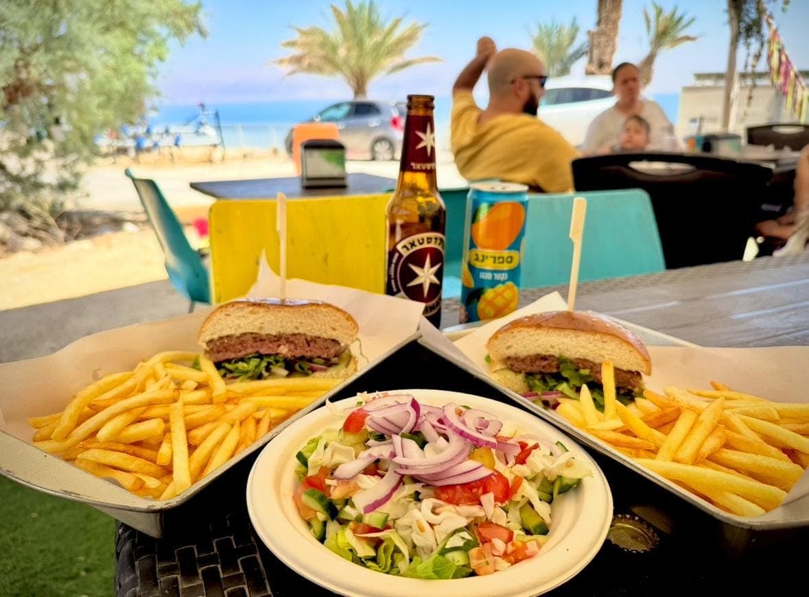 שני המבורגרים עם צ'יפס וסלט על השולחן, מול הנוף של ים המלח
